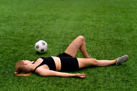 Téléchargez les photos : Football féminin fatigué joueur de football féminin couché terrain de gazon synthétique vert au repos après un entraînement dur ou match - en image libre de droit