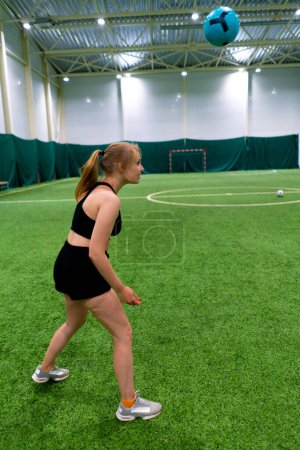 Foto de Fútbol femenino joven niña entrena coordinación en el campo de fútbol interior golpeando la pelota con la cabeza - Imagen libre de derechos