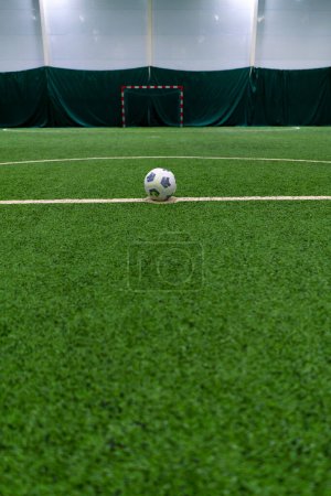 Foto de Una pelota de fútbol blanco y negro se encuentra en un campo de deportes en un césped sintético verde antes del inicio del juego deportivo - Imagen libre de derechos