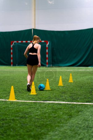 Photo for Young girl is training on the soccer field driving the ball between the chips or cones preparing for match - Royalty Free Image