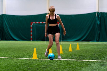 Photo for Young girl is training on the soccer field driving the ball between the chips or cones preparing for match - Royalty Free Image
