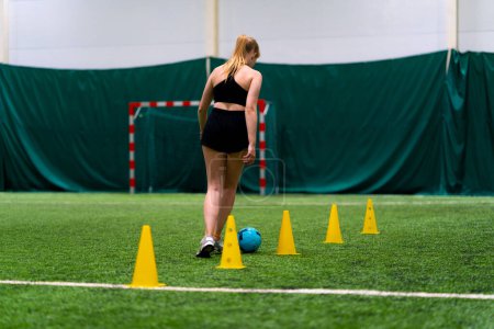 Téléchargez les photos : Jeune fille s'entraîne sur le terrain de football conduisant le ballon entre les puces ou les cônes se préparant pour le match - en image libre de droit
