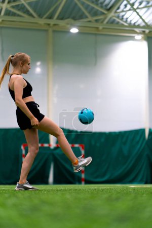 Téléchargez les photos : Jeune fille s'entraîne sur le terrain de football en donnant des coups de pied au ballon en le jetant dans l'air en améliorant ses compétences sportives - en image libre de droit