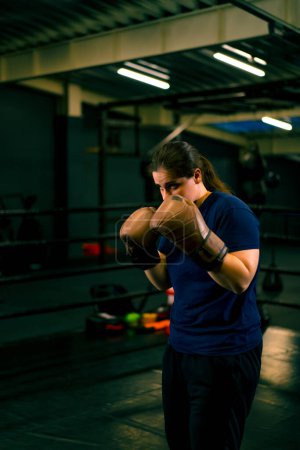 Photo for Portrait of a woman in boxing gloves posing in a cheeky and competitive fight in a boxing ring before fight with an opponent - Royalty Free Image