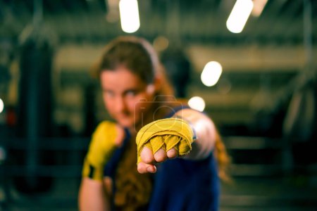 Téléchargez les photos : Portrait concentré Boxer fille en bandages de boxe jaune debout dans une position de boxe sur un fond sombre dans la salle de gym avant un combat - en image libre de droit