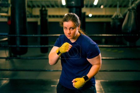 Foto de Retrato enfocado Boxer chica en vendas de boxeo amarillo de pie en una postura de boxeo sobre un fondo oscuro en el gimnasio antes de una pelea - Imagen libre de derechos
