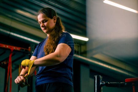 Photo for Sporty girl with strong arms prepares for a hard workout wraps a bandage on her fists to protect her fingers in gym - Royalty Free Image
