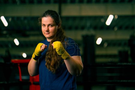 Foto de Retrato enfocado Boxer chica en vendas de boxeo amarillo de pie en una postura de boxeo sobre un fondo oscuro en el gimnasio antes de una pelea - Imagen libre de derechos