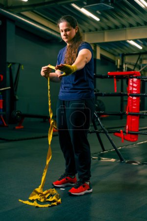 Foto de Deportiva chica con los brazos fuertes se prepara para un entrenamiento duro envuelve un vendaje en sus puños para proteger sus dedos en el gimnasio - Imagen libre de derechos