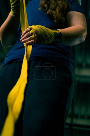Photo for Sporty girl with strong arms prepares for a hard workout wraps her fists with a bandage to protect her fingers in gym close-up - Royalty Free Image
