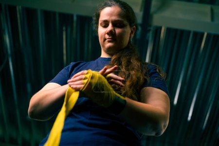 Foto de Deportiva chica con los brazos fuertes se prepara para un entrenamiento duro envuelve un vendaje en sus puños para proteger sus dedos en el gimnasio - Imagen libre de derechos