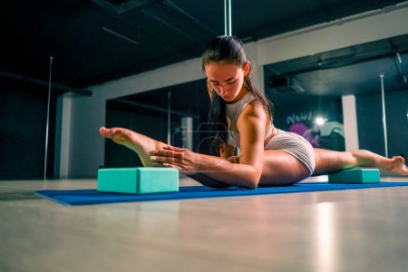 Foto de Joven hermosa chica flexible entrenador haciendo estiramiento antes de polo baile sentado twine entrenamiento deporte - Imagen libre de derechos