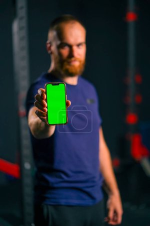 Foto de Hombre entrenador de fitness mostrar el teléfono con pantalla verde deporte estilo de vida tecnología de entrenamiento - Imagen libre de derechos