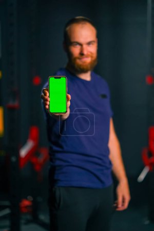 Foto de Hombre entrenador de fitness mostrar el teléfono con pantalla verde deporte estilo de vida tecnología de entrenamiento - Imagen libre de derechos