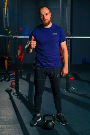 Photo for Portrait of a satisfied athlete in the gym after a workout, a man shows super sign with his hand calls for a sports lifestyle - Royalty Free Image