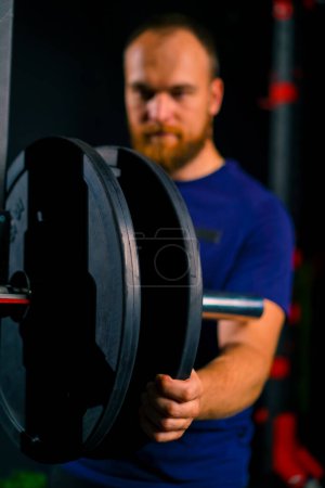 Photo for Male athlete trainer adds weight to the barbell in the gym increases the load on the body of bodybuilder - Royalty Free Image