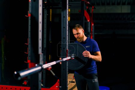 Foto de Entrenador atleta masculino añade peso a la barra en el gimnasio aumenta la carga sobre el cuerpo del culturista - Imagen libre de derechos