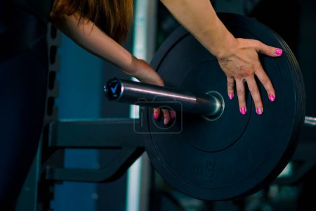 Foto de Primer plano de las manos de una atleta femenina añadiendo pesos a la barra en el gimnasio - Imagen libre de derechos
