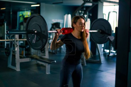 Téléchargez les photos : Portrait d'une femme de fitness concentrée faisant un exercice de presse d'épaule lourde avec un haltère dans les groupes musculaires de formation de gymnase - en image libre de droit