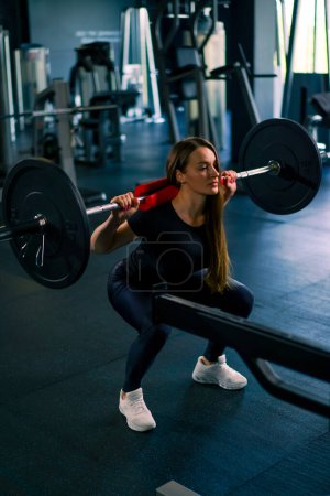 Foto de Retrato de una mujer de fitness concentrada haciendo un ejercicio de presión de hombro pesado con una barra en grupos musculares de entrenamiento de gimnasio - Imagen libre de derechos