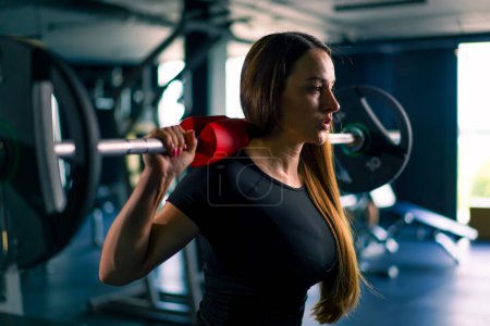 Photo for Portrait of a concentrated fitness woman doing a heavy shoulder press exercise with a barbell in gym training muscle groups - Royalty Free Image