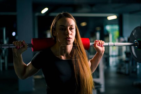 Foto de Retrato de una mujer de fitness concentrada haciendo un ejercicio de presión de hombro pesado con una barra en grupos musculares de entrenamiento de gimnasio - Imagen libre de derechos