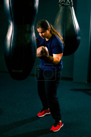 Foto de Una chica boxeadora con guantes resuelve el poder de los golpes en un saco de boxeo en el gimnasio entrena duro antes de luchar - Imagen libre de derechos