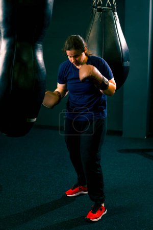 Foto de Una chica boxeadora con guantes resuelve el poder de los golpes en un saco de boxeo en el gimnasio entrena duro antes de luchar - Imagen libre de derechos