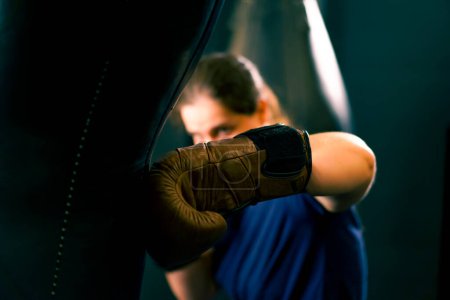 Téléchargez les photos : Un boxeur de fille dans des gants travaille sur la force des coups de poing sur un sac de boxe dans le gymnase s'entraîne dur avant de se battre gros plan - en image libre de droit
