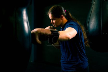 Photo for A girl boxer in gloves works out the power of punches on a punching bag in the gym trains hard before fight - Royalty Free Image