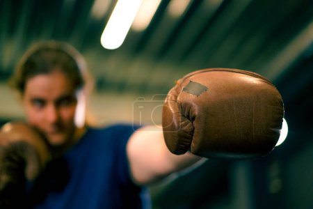 Téléchargez les photos : Femme en gants de boxe posant dans un combat sassy et compétitif dans un ring de boxe avant un combat avec l'adversaire gros plan - en image libre de droit