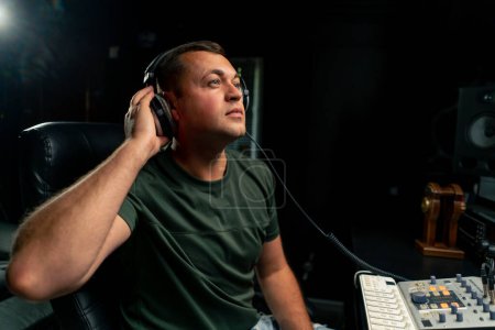 Téléchargez les photos : Un ingénieur du son masculin concentré portant un casque s'assoit à un bureau de mixage pour enregistrer une nouvelle piste - en image libre de droit