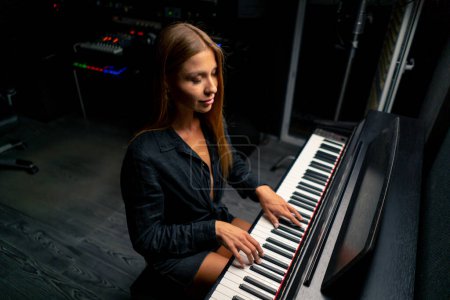 Photo for Female pianist preparing for a concert and playing a lyrical melody on the piano keys in a music studio - Royalty Free Image