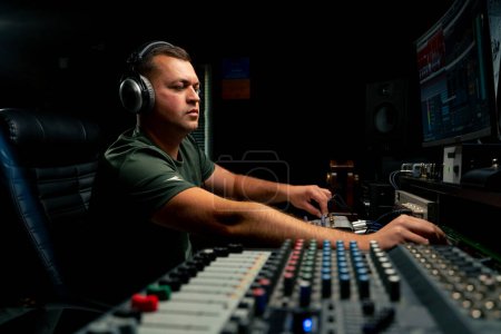 Foto de Un ingeniero de sonido masculino enfocado que usa auriculares se sienta en un escritorio de mezcla grabando una nueva pista - Imagen libre de derechos