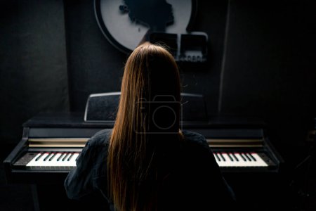 Photo for Long-haired girl composer sits with her back to the camera and plays the piano in a recording studio - Royalty Free Image