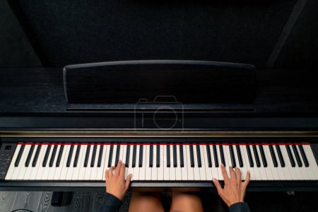 Foto de El plano de arriba es de una joven sentada al piano y tocando una hermosa melodía lírica - Imagen libre de derechos