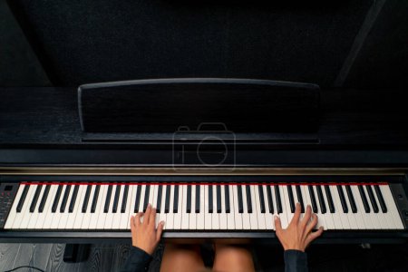 Foto de El plano de arriba es de una joven sentada al piano y tocando una hermosa melodía lírica - Imagen libre de derechos