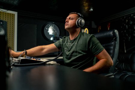 Photo for A focused male sound engineer wearing headphones sits at a mixing desk recording a new track - Royalty Free Image