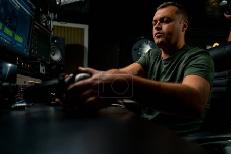 Téléchargez les photos : Un ingénieur du son masculin concentré portant un casque s'assoit à un bureau de mixage pour enregistrer une nouvelle piste - en image libre de droit