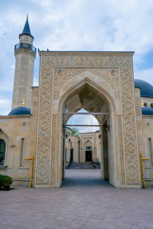 Téléchargez les photos : Belle entrée cosy d'une mosquée musulmane entourée d'une arche avec des ornements islamiques contre le ciel bleu - en image libre de droit