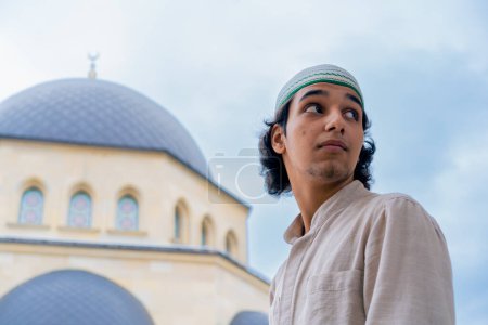 Téléchargez les photos : Gros plan du visage d'un jeune Arabe sur fond de grande mosquée musulmane et de ciel bleu - en image libre de droit