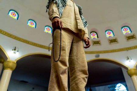 Foto de Disparo por la espalda Un hombre musulmán se para en la alfombra en medio de la sala de oración en la mezquita con la cabeza levantada - Imagen libre de derechos