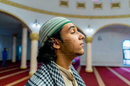 Téléchargez les photos : Gros plan du visage d'un musulman debout sur un tapis au milieu d'une salle de prière dans une mosquée, la tête levée - en image libre de droit