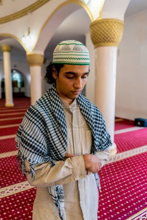 Foto de Un joven musulmán con ropa árabe nacional reza en una mezquita durante las vacaciones del Ramadán - Imagen libre de derechos
