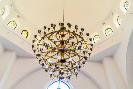 Foto de Una hermosa lámpara de araña de oro de lujo cuelga en la sala de una mezquita musulmana en un techo blanco - Imagen libre de derechos