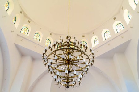 Foto de Una hermosa lámpara de araña de oro de lujo cuelga en la sala de una mezquita musulmana en un techo blanco - Imagen libre de derechos