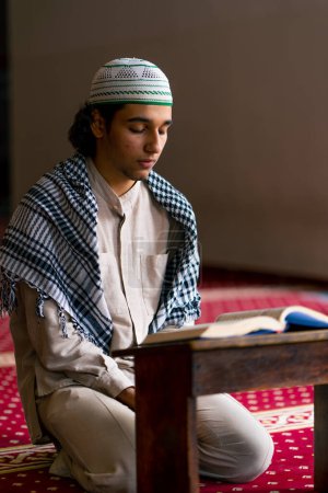 Téléchargez les photos : Un musulman assis en silence sur le tapis de la mosquée sainte prie le Coran et se tourne vers Allah - en image libre de droit