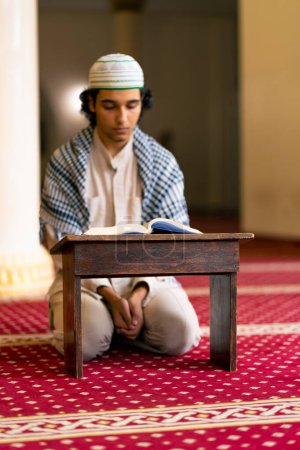 Téléchargez les photos : Un musulman assis en silence sur le tapis de la mosquée sainte prie le Coran et se tourne vers Allah - en image libre de droit