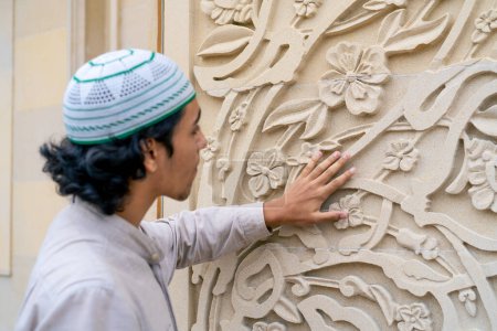 Téléchargez les photos : Un musulman examine avec enthousiasme l'ornement islamique sur l'arche à l'entrée de la mosquée - en image libre de droit