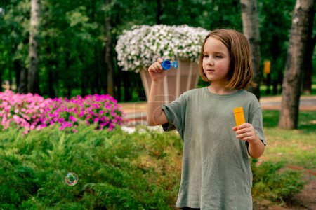 Photo for Portrait beautiful cute little girl blowing soap bubble in city park happy carefree childhood - Royalty Free Image
